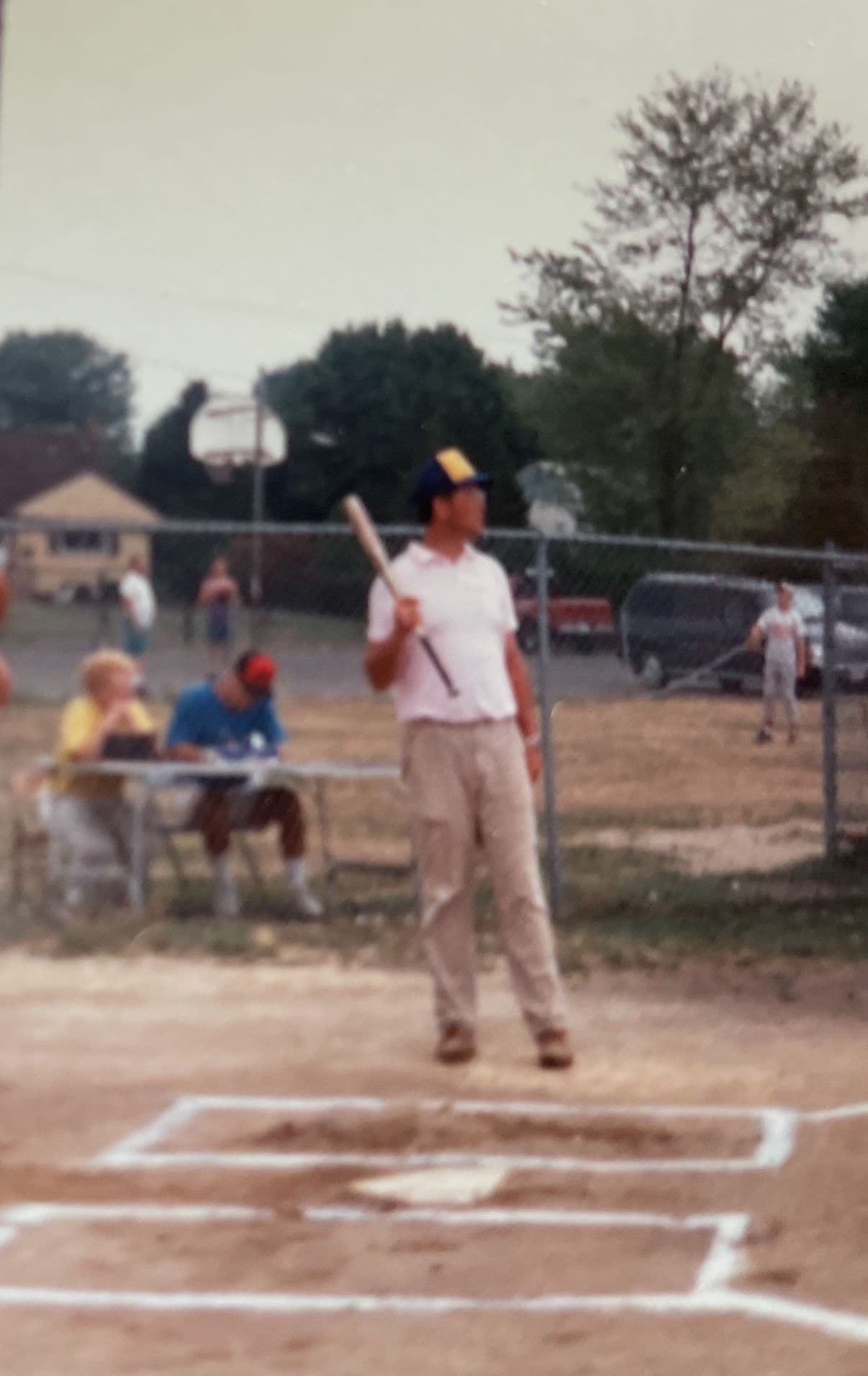 A batter at the plate, bat held high, on a neighborhood ballfield